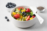 Pieces of mango, strawberries, blueberries, kiwi and mint in white bowl. Fruity fresh raw summer salad