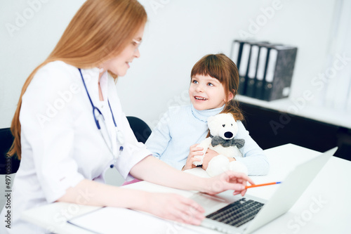 Fototapeta Naklejka Na Ścianę i Meble -  Online medicine. Female doctor and little girl patient use laptop in office hospital