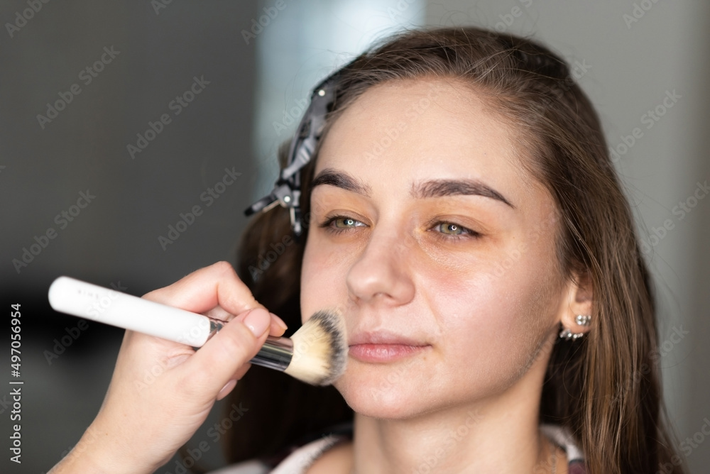 Obraz premium Makeup artist distributes foundation on the girl's face with a brush