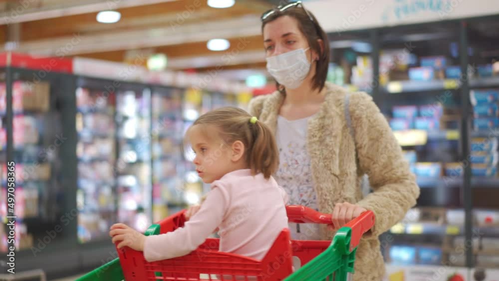 Child, little girl 5 years sitting shopping cart in supermarket while mother choose goods to buy it Female kid with mother in shopping cart food store or supermarket. Little kid going shopping.