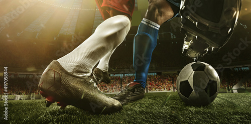 Fototapeta Naklejka Na Ścianę i Meble -  Close-up legs of soccer, football players in action, motion at the stadium with flashlights and crowded stands. Concept of sport, competition, movement, overcoming.
