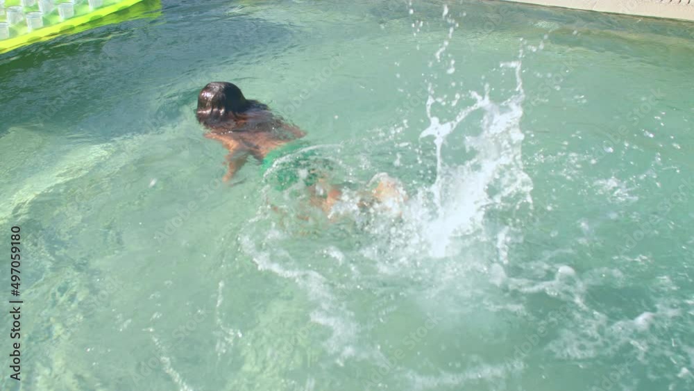 A child jumps into an outdoor pool, splashes a lot, swims underwater, actively moving his legs. Water play allows children to explore and a confidence booster for kids.