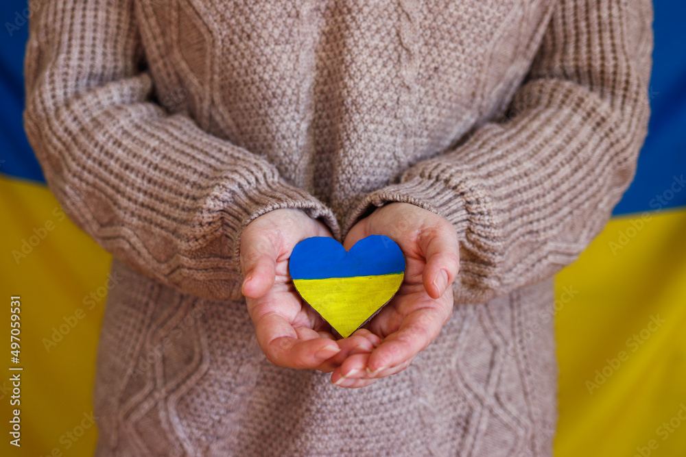 Woman holding heart shape in colors of ukrainian flag. Protest against war at Ukraine. Peace and love concept