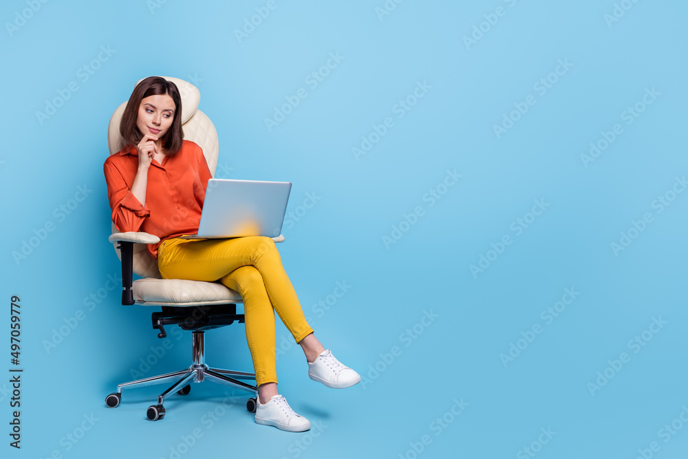 Portrait of attractive minded girl sitting in armchair using laptop deciding copy space isolated over bright blue color background