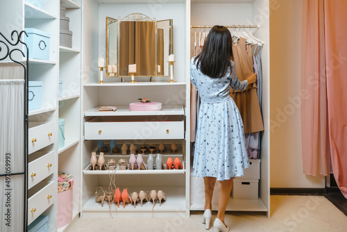 Attractive woman choosing a dress in a dressing room or store. View from the back. Fashion, style and space organization concept