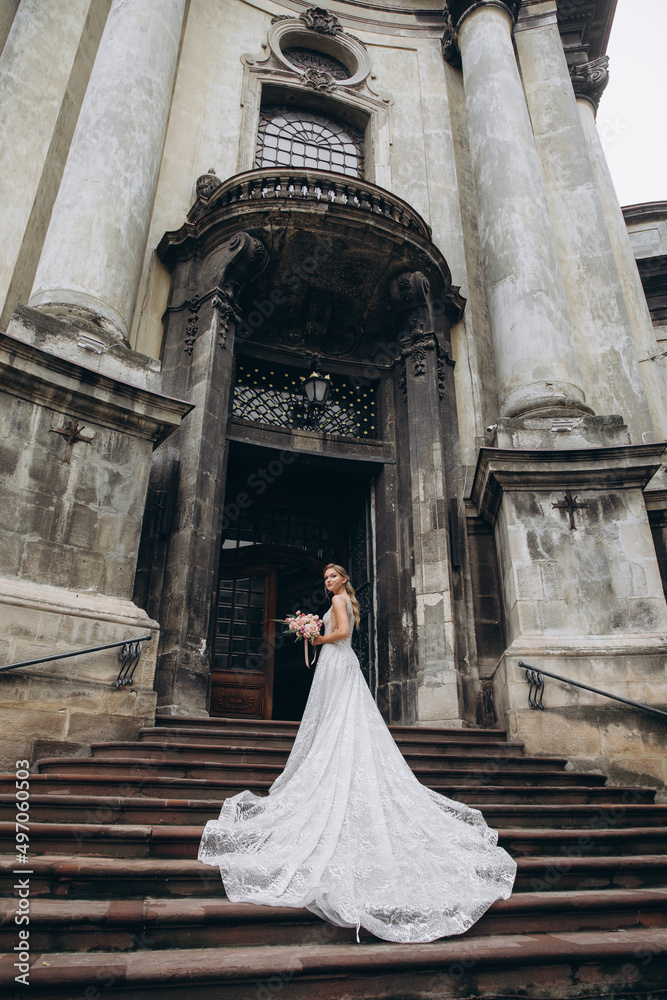 Bride in dress with long train stands before an old Gothic church