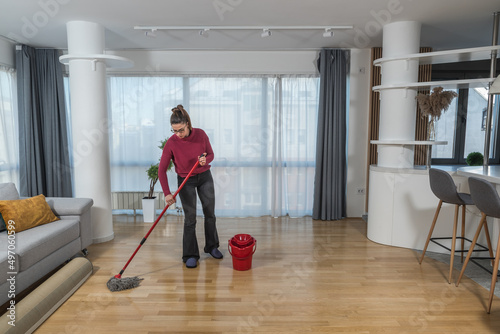 Young woman cleaning her apartment floor with mop and wet wipe. Female doing housework and maintaining hygiene of clean home to remove dust and dirt.