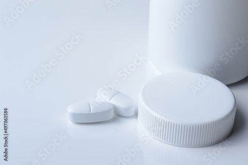 white plastic medicine jar and two white pills. light background