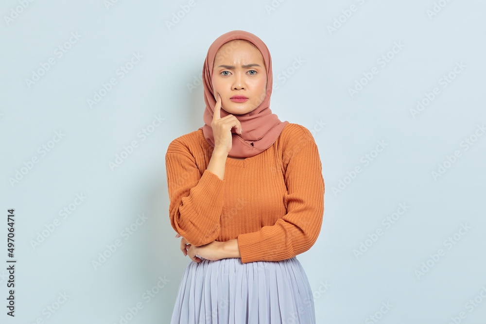 Portrait of beautiful young Asian Muslim woman in brown sweater and looking serious thinking about question and looking at camera isolated on white background. Muslim lifestyle concept Portrait of beautiful young Asian Muslim woman in brown sweater and looking serious thinking about question and looking at camera isolated on white background. Muslim lifestyle concept