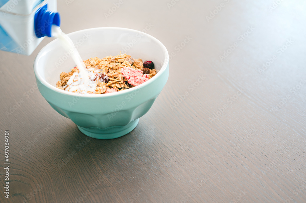Milk pouring into bowl of fresh muesli, side view with copy space, isolated on wooden background. Healthy breakfast concept. Milk pouring into bowl of fresh muesli, side view with copy space, isolated on wooden background. Healthy breakfast concept.