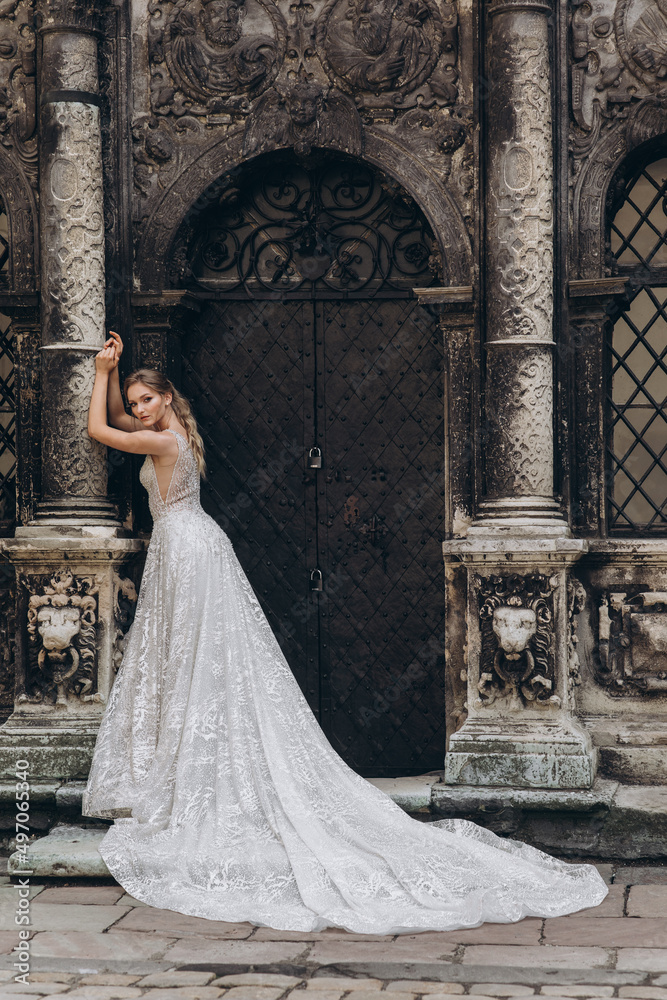 Beautiful bride in a long white wedding dress on a background of black old building