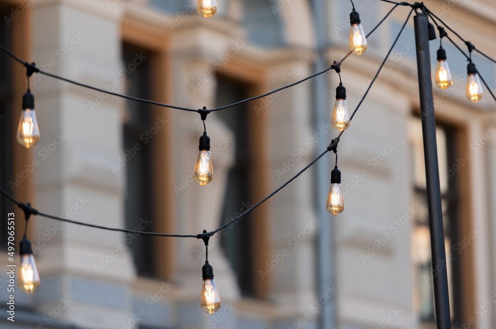 a row of electric light bulbs hang against a blurred old city background
