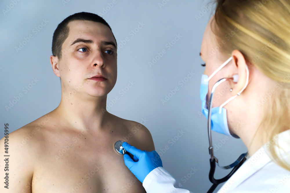 Young man at the doctor's office. The doctor, a young woman, carefully listens to his heart, lungs with a phonendoscope. Family doctor. Young man at the doctor's office. The doctor, a young woman, carefully listens to his heart, lungs with a phonendoscope. Family doctor.