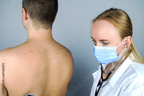 Young man at the doctor's office. The doctor, a young woman, carefully listens to his heart, lungs with a phonendoscope. Family doctor.