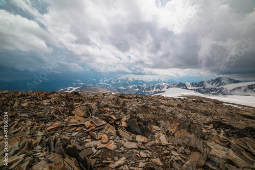 Awesome alpine scenery with snow mountains under cloudy sky. Scenic mountain landscape at very high altitude in overcast. Beautiful atmospheric view from sharp stone hill to snowy mountain range.