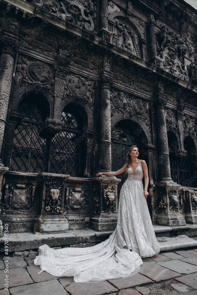 Charming bride in a long white wedding dress on a background of black old building
