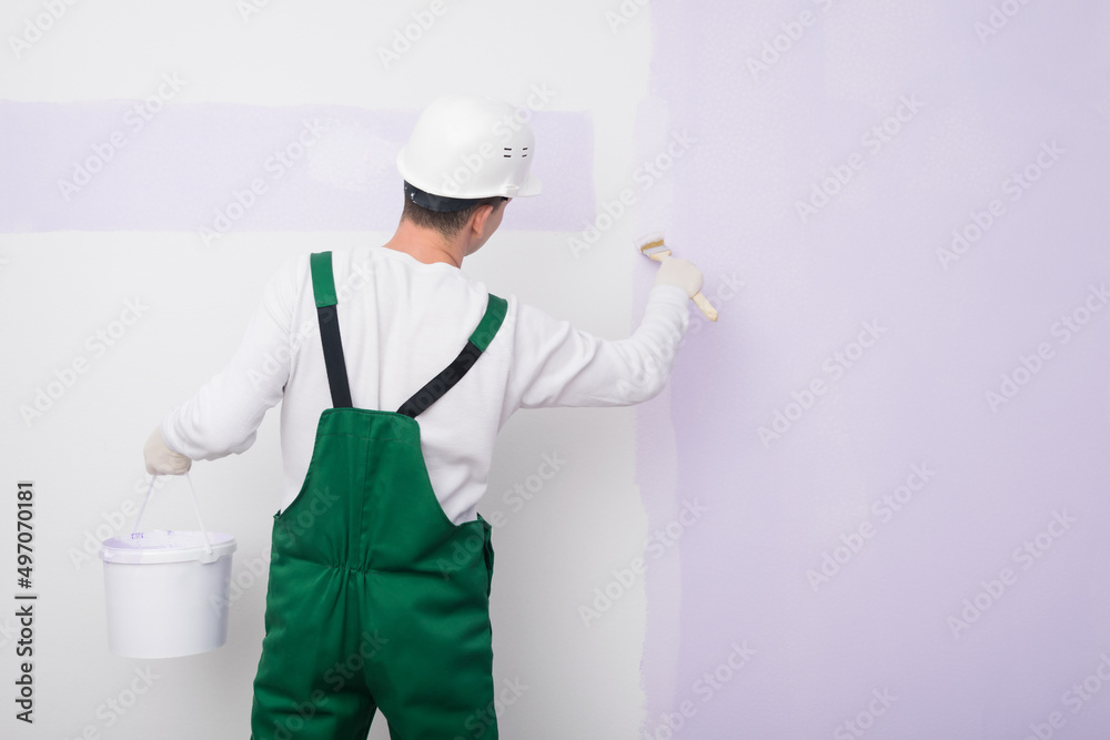 a worker in a white helmet paints a white wall in a different color a worker in a white helmet paints a white wall in a different color