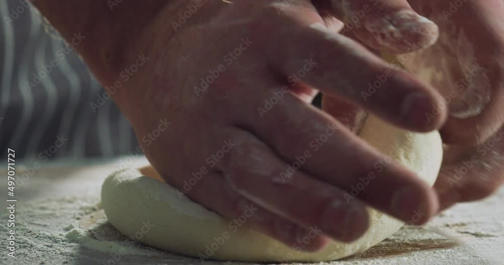 Cinematic macro shot of professional artisan baker chef kneading just prepared loaf of dough for better levitation for preparation of pasta, pizza and other pastries in rustic bakery kitchen.