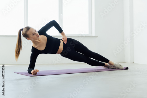 Fitness woman side plank workout training at white background indoors. Young slim girl makes exercise.