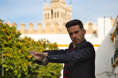 gypsy man dancing flamenco, dressed in black with castanets is posing with his arms up among orange trees and in the background the giralda of seville. Flamenco cultural heritage of humanity photo