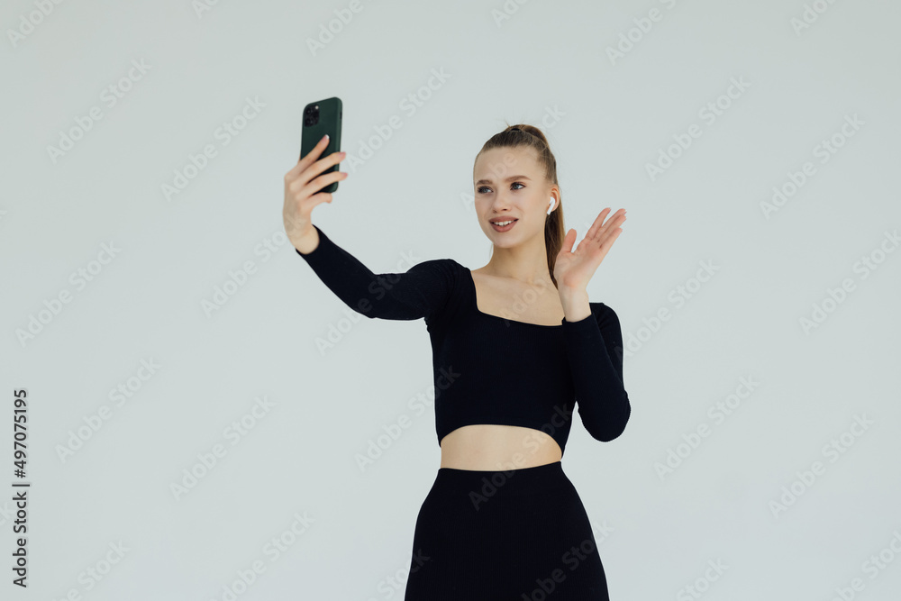 Young woman making video call and pointing gladly at camera of her phone over white background