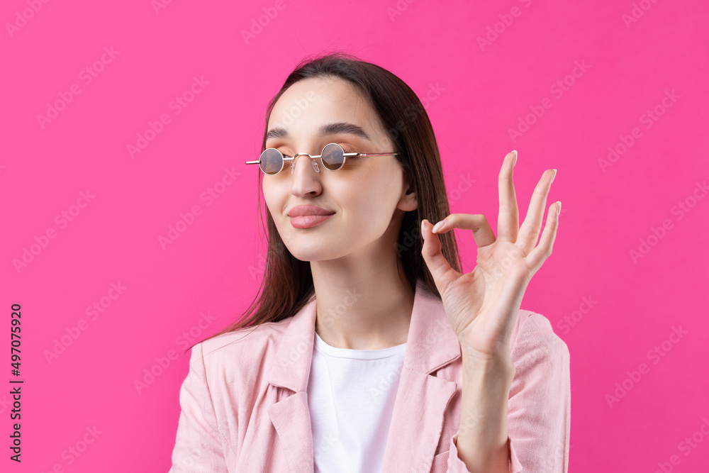 Portrait of beautiful young woman in pink jacket thinking isolated on red background. Shows an OK sign. Portrait of beautiful young woman in pink jacket thinking isolated on red background. Shows an OK sign.