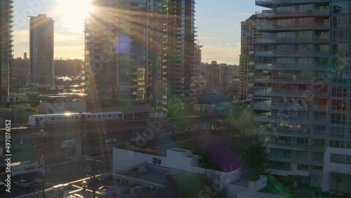 Sun Shining Behind High-rise Building At Dusk With Train On Railway In Canada. - aerial photo