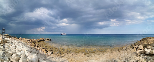 Panorama. The stone coast of the Mediterranean Sea, a white ship in the sea and the largest sailing yacht in the world against a dramatic sky.
