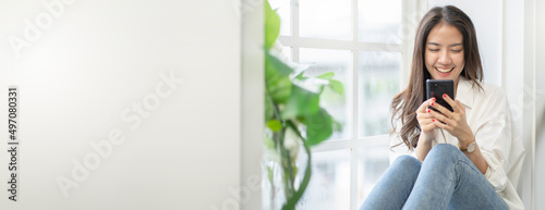 music streaming concept.look at camera of Serene young asian woman wearing headphones and relaxing beside window.happy lady enjoys listening chill music streaming online,audio sound at home.
