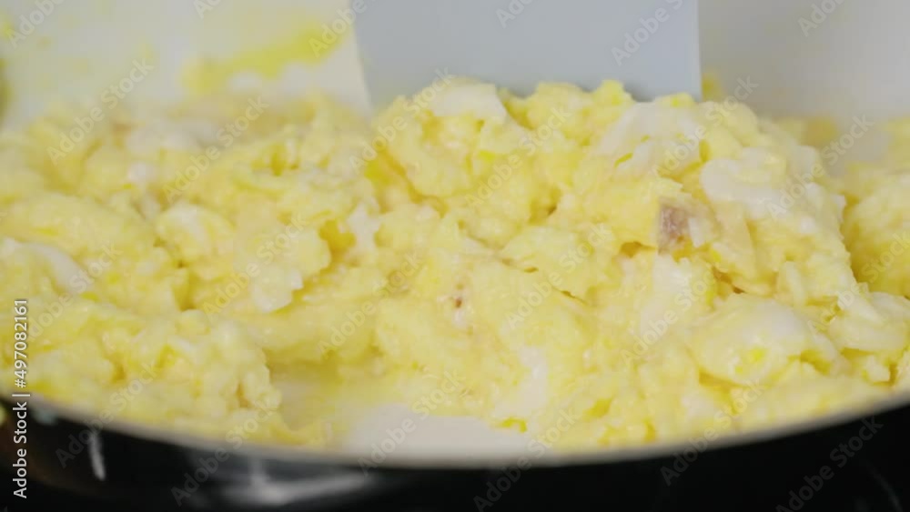 Cooking scrambled eggs for breakfast in a white pan with spatula close up slow motion in 4k