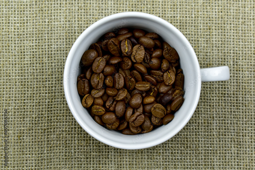 white cup filled with coffee beans, standing on burlap, top view, close-up white cup filled with coffee beans, standing on burlap, top view, close-up