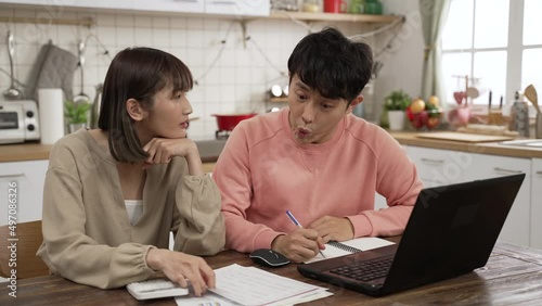 worried Asian husband and wife examining tax bills and calculating spending with a calculator at home. the man feeling shocked about going over budget
