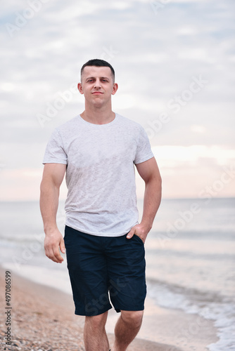 Young handsome smiling guy walks by the sea on the sand in summer © Юлія Блоха