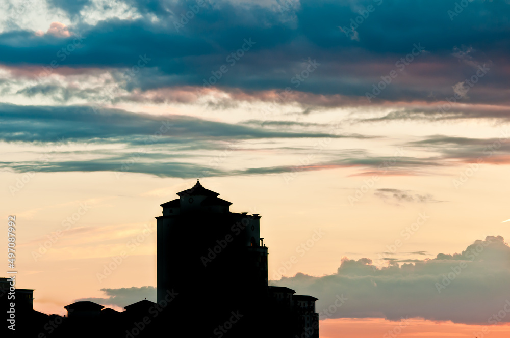 front view, far distance of, a tall building in silhouette, against a sunset with a huge gray cloud