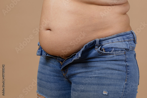 Woman with flabby belly and thick sides showing waist in unzipped jeans of blue color. Sudden weight gain. Visceral fat. Body positive. Tight little clothes. Need for wardrobe change.