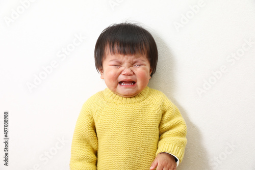 黄色いセーターを着た泣いている女の子（幼児）の写真。