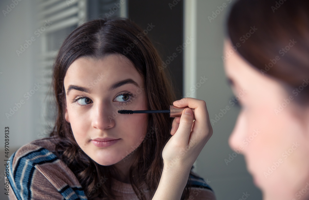 A young woman paints her eyelashes with mascara in front of a mirror. A young woman paints her eyelashes with mascara in front of a mirror.