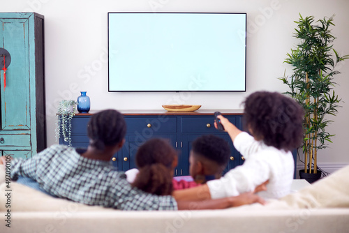 Rear View Of Family Sitting On Sofa Watching Movie On TV At Home