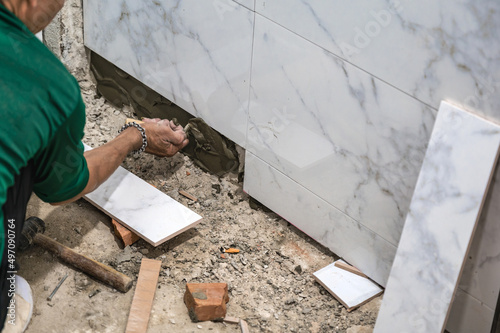 Male tiler using trowel laying marble tile with cement in bathroom. Housing development, improvement renovation