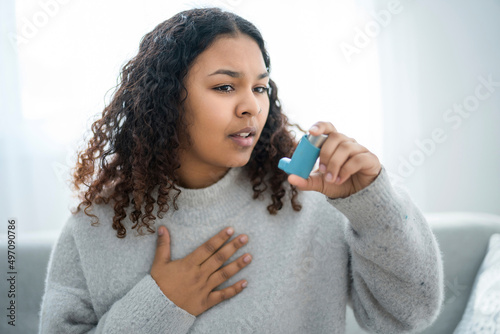 black woman taking her inhaler at home at the living room photo