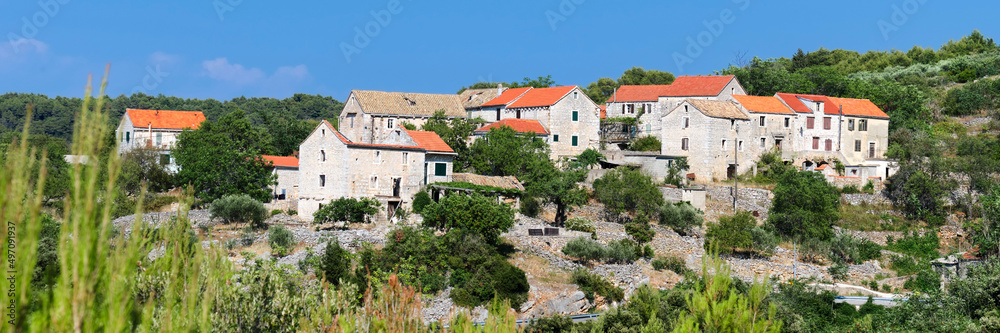 Old village in mountains of Hvar island in Croatia. Panoramic banner image. Old mountain road between coastal towns. Old stone cottage houses under red tile roofs.