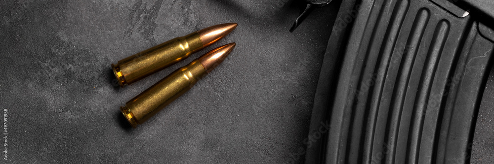 Two bullets and Kalashnikov assault rifle on gray concrete background banner, top view panoramic web header. Cartridge 7.62 caliber for ak 47. Wide screen wallpaper Two bullets and Kalashnikov assault rifle on gray concrete background banner, top view panoramic web header. Cartridge 7.62 caliber for ak 47. Wide screen wallpaper