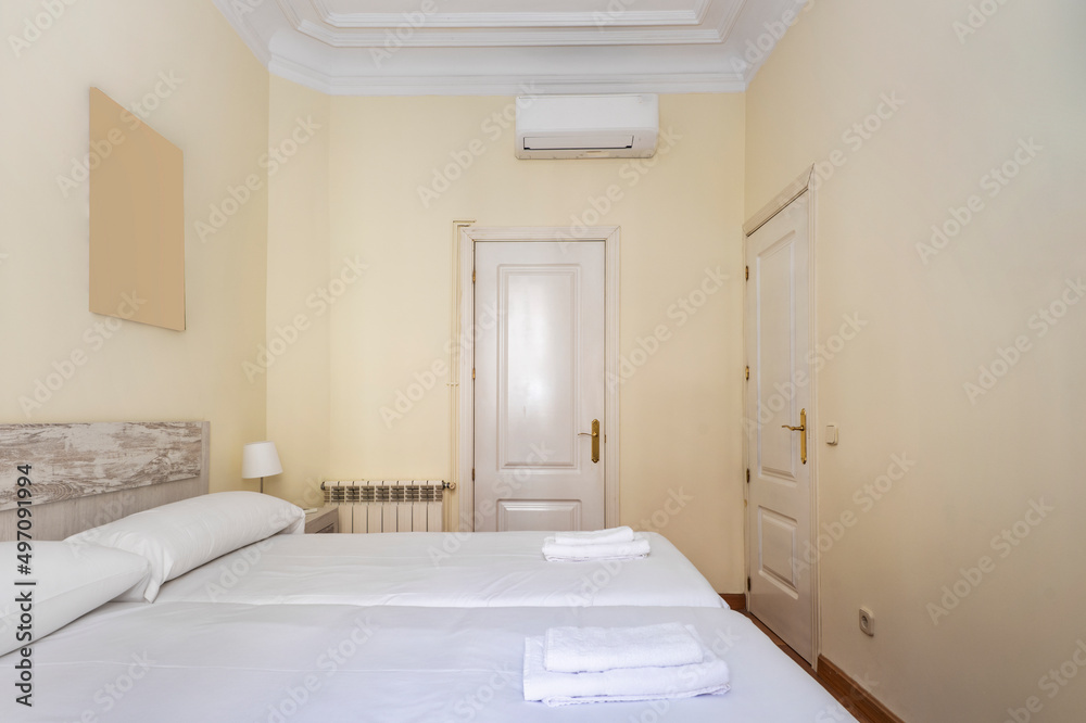 bedroom with two beds together with white bedding, wooden headboard and white lacquered carpentry