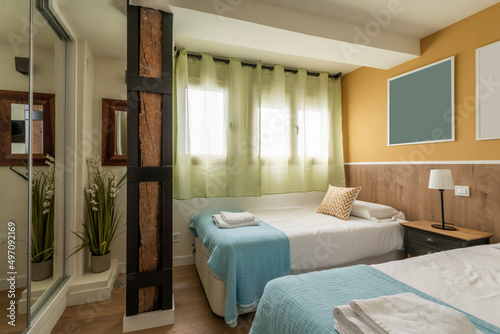 Bedroom with youthful beds with blue bedspreads, green net curtains and built-in wardrobe with sliding mirror doors