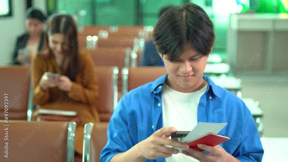 Young Asian man use mobile phone to surf internet and enjoy also hold passport and boarding pass during wait to check-in at gate of airport. Young Asian man use mobile phone to surf internet and enjoy also hold passport and boarding pass during wait to check-in at gate of airport.