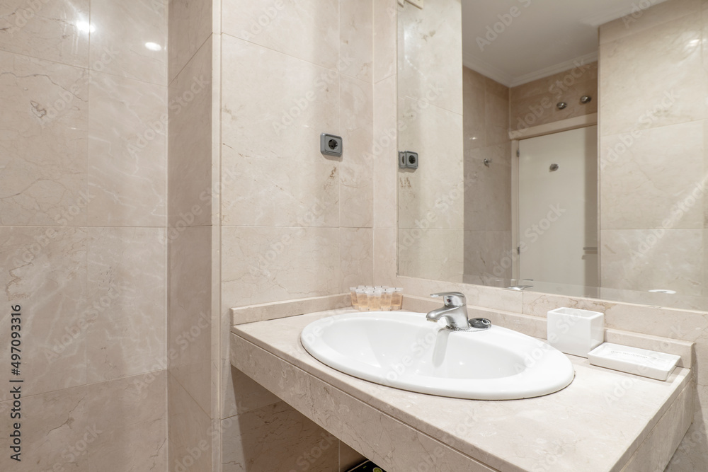 bathroom with white porcelain sink on marble countertop, cream marble walls and wall mounted frameless mirror in vacation rental apartment bathroom with white porcelain sink on marble countertop, cream marble walls and wall mounted frameless mirror in vacation rental apartment