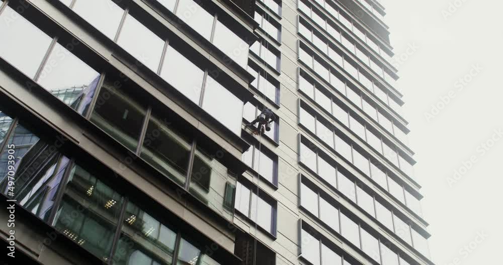 A man hanging from cables washes the windows from the outside of building A man hanging from cables washes the windows from the outside of building