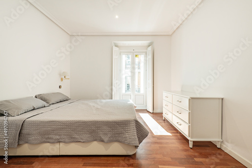 Bedroom with double bed with gray bedspread  white wooden chest of drawers and balcony with wooden shutters