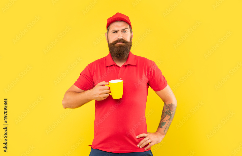 Fototapeta premium Serious bearded man in casual red cap and tshirt holding mug yellow background, tea