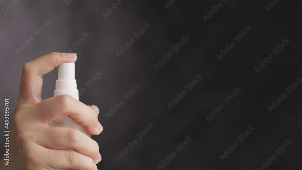 close up woman hand holding small spray bottle and spraying on dark background
